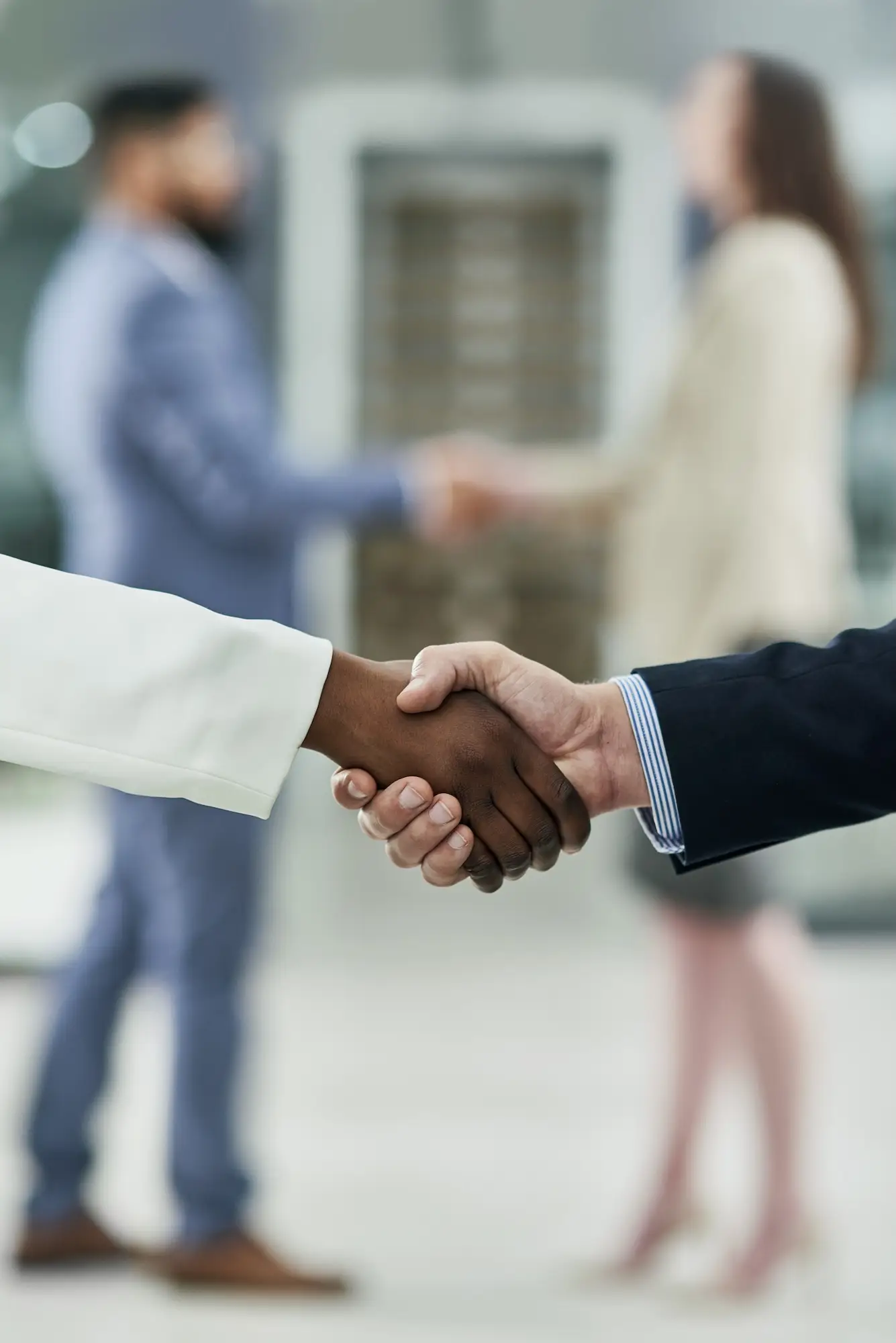 Two people shaking hands in the foreground with two more people out of focus shaking hands in the background