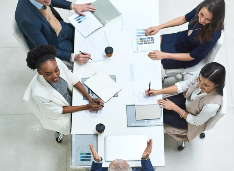 An overhead view of five professionals seated around a table talking.